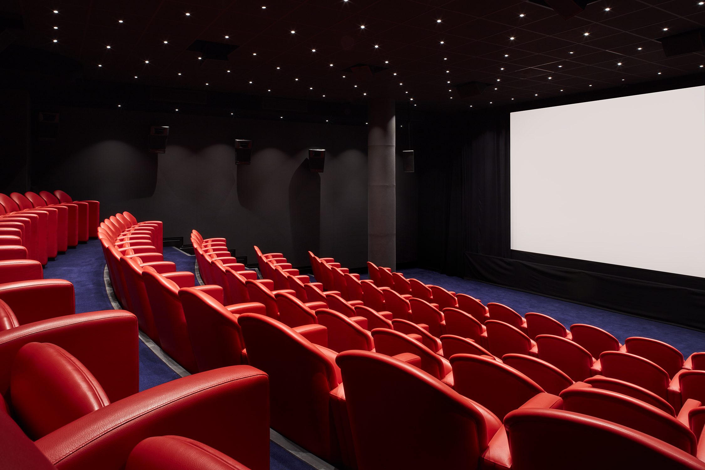 Large screening room at Soho Hotel. Tiered rows of red leather seats face towards a blank cinema screen.